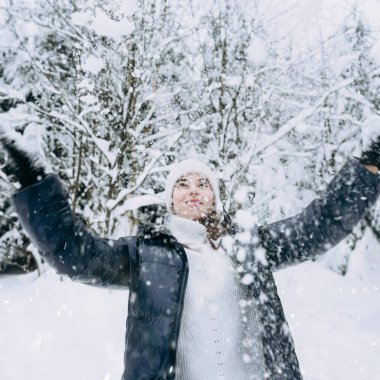 Genç, mutlu, güzel bir kız kış parkında havaya beyaz kar fırlatıyor. Kış hayatı. Özel kış maceraları. Yerel seyahat. Sağlıklı mola.
