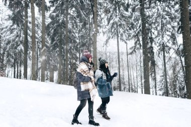 Sıcak kış kıyafetleri içinde iki aktif genç turist, karla kaplı güzel bir manzaranın arka planında yürüyor. Yürüyüş. Kişisel maceralar. Yerel seyahat.