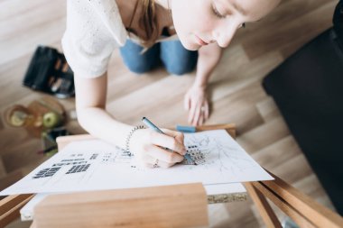 Modern bir iç mekanda genç bir kız öğrencinin üst görüntüsü. Bir mimari proje için bir skeç çizer, bir kalem ve resim kullanır. Pandemic sırasında evde eğitim ve eğitim kavramı. COVID-19