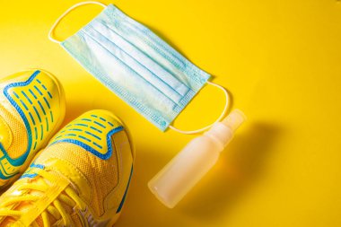 Spor ayakkabıları, cerrahi maske ve sarı arka planda hidroseksüel jel. Ev zindeliği ve yeni normallik kavramı. Yatay fotoğrafçılık