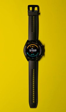 Sarı bir arkaplanda siyah bir akıllı yamaca yakın dur, tıpkı bir saat yüzü gibi. Teknoloji ve spor konsepti. Dikey fotoğrafçılık. Boşluğu kopyala