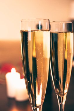 Arka planda odağını kaybetmiş mumlarla iki kadeh şampanyayı yakından çek. Evde romantik sevgililer günü yemeği kavramı, yeni normal. Dikey fotoğrafçılık
