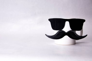 Bıyıklı ve renkli konfetilerin üzerinde gözlüklü beyaz bir kupa. Babalar günü konsepti. Boşluğu kopyala