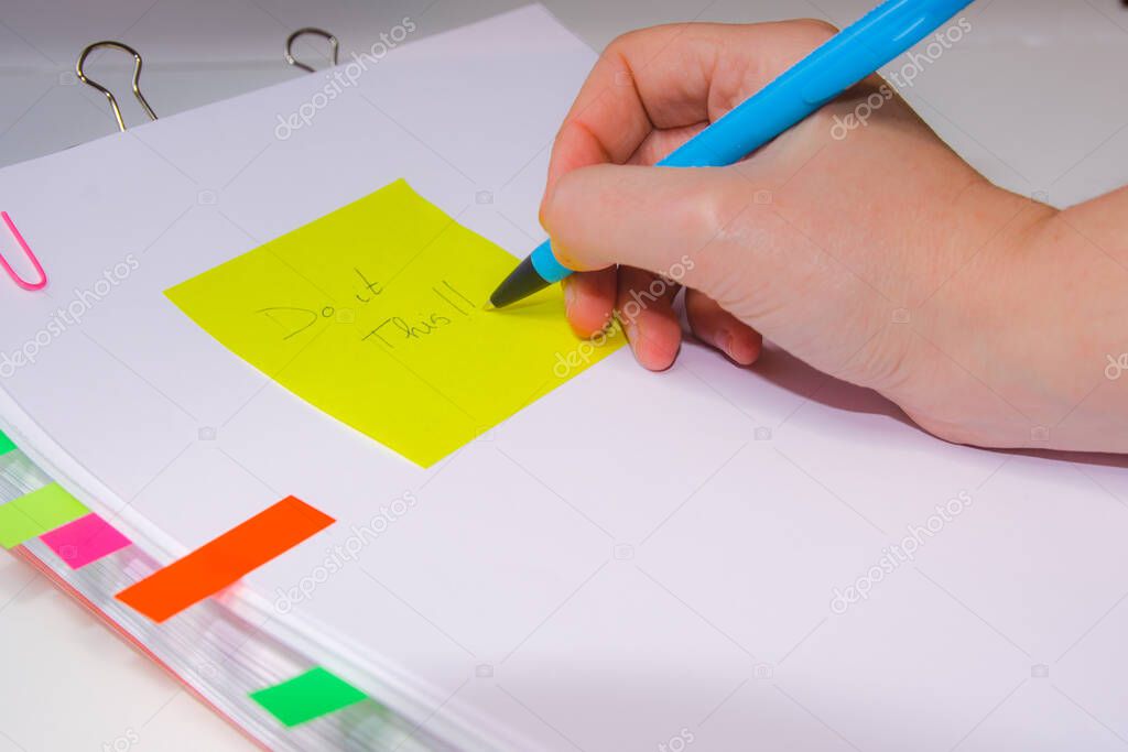 Close-up of a hand writing on a yellow paper. Horizontal photography. Information overload concept