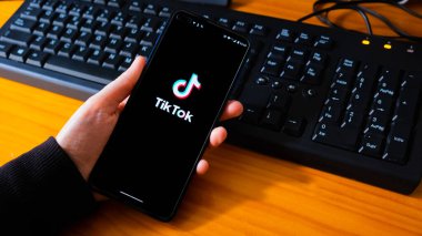 İspanya, 04, 08, 2021. Siyah arka planda TikTok logosu olan el ele tutuşan telefon. Tiktokerların milyonlarca hayranı var..