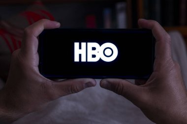 İspanya. 04, 18, 2021. Akşamları koltuğunda HBO ekranı olan akıllı telefon tutan bir adamın yakın çekimi.