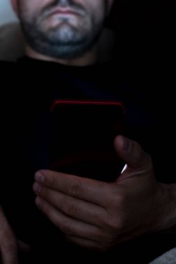Akşamları kanepede oturan bir adamın akıllı telefonu kullanışının yakın çekimi. Uykusuzluk konsepti. Gece mobil aygıtların kullanımı