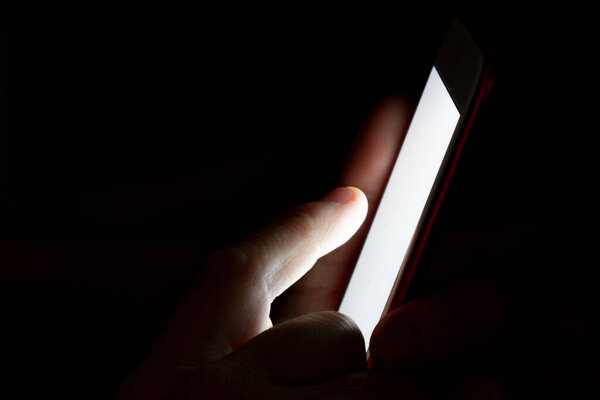 Close-up of a man lying down at night making use of the smartphone. Insomnia concept. Use of mobile devices at night