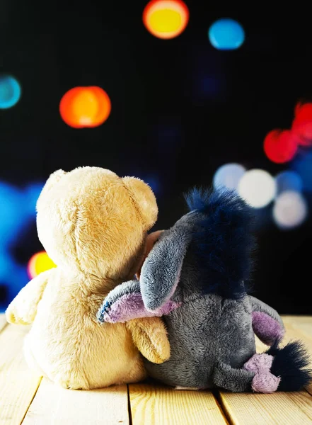 Two teddy bears hugging their backs on a wooden table and defocused lights background. Tender friendship concept. International Friendship Day