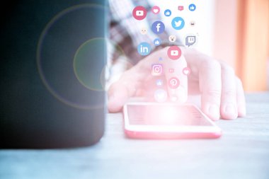 Akıllı telefon kullanan, sosyal medya logoları ve simgeleri telefondan çıkan genç bir adam. İletişim ve ağ konsepti. Çift pozlama