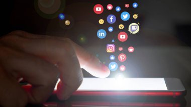 Akıllı telefon kullanan, sosyal medya logoları ve simgeleri telefondan çıkan genç bir adam. İletişim ve ağ konsepti. Çift pozlama