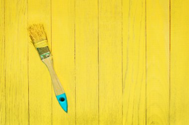 Brush in yellow paint on blue and yellow wooden background