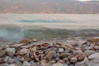 Lago di Garda (Garda Gölü) gün batımında açık pembe ile arka planda bir dağ. Uzun süre maruz kalma süresi - küçük dalgalar 