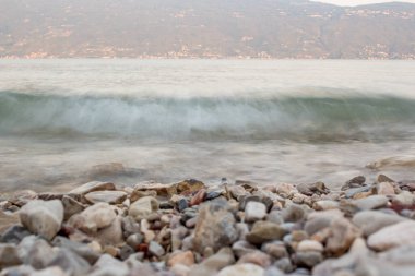 Lago di Garda (Garda Gölü) gün batımında açık pembe ile arka planda bir dağ. Uzun süre maruz kalma süresi - küçük dalgalar 