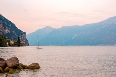 Lago di Garda (Garda Gölü) gün batımında açık pembe ile arka planda bir dağ. Uzun süre maruz kalma süresi - küçük dalgalar 