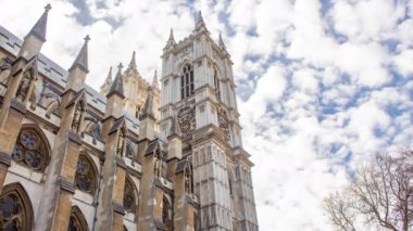 Güneşli bir günde Londra 'daki Westminster Manastırı' nın zaman aşımı. Yakınlarda bir kule ve arkada bulutlar var.