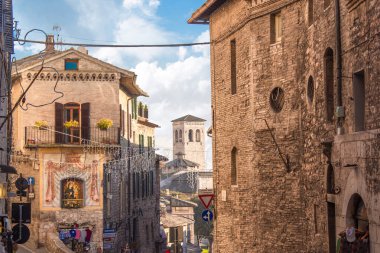 Günbatımında bulutlu bulutlu gökyüzü ve arka planda ortaçağ kulesiyle İtalya 'nın Umbria ilindeki Assisi kasabasının şehir manzarası