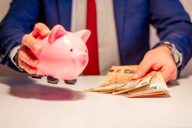Elindeki 50 Euro 'luk banknotla elinde domuz kumbarası tutan bir iş adamı. Finansal ve para tasarrufu kavramı