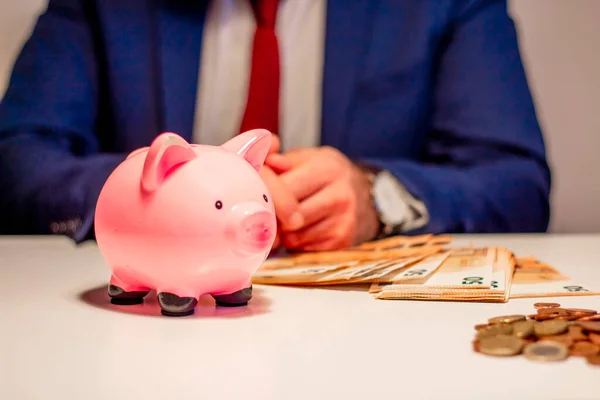 İşadamı 50 Euro 'luk banknot sayıyor, kumbaraya yakın. Finansal ve para tasarrufu kavramı
