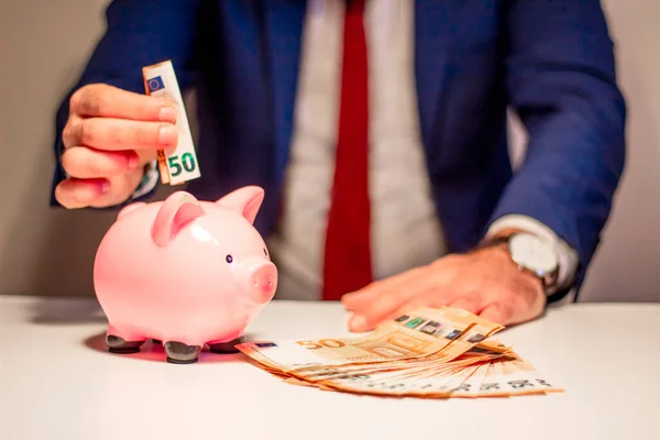 İşadamı domuz kumbarasına 50 euro yatırıyor. Finansal ve tasarruf para kavramı