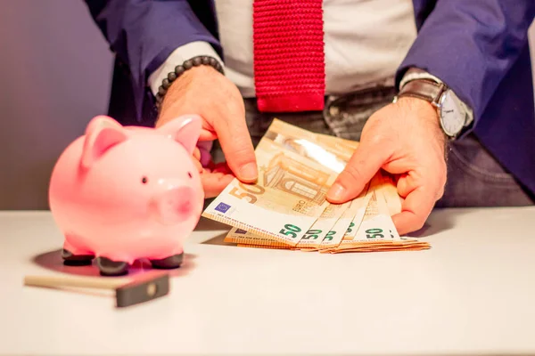 Elindeki elli avroluk banknotla iş adamı, yakın planda domuz kumbarası. Finansal ve para tasarrufu kavramı