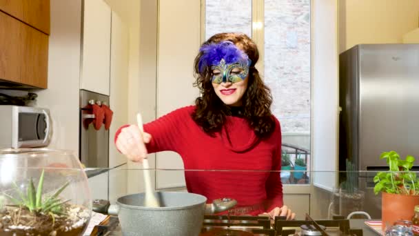 Hübsche Frau kocht während des Karnevals in venezianischer Karnevalsmaske Suppe auf Herd in der Küche. Nahaufnahme einer Hausfrau, die zu Hause das Abendessen zubereitet