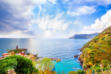 Liguria 'da Akdeniz kıyısındaki dağdaki Cinque Terre' de Vernazza - İtalya ve güneşli bulutlu gökyüzü. Geleneksel İtalyan mimarisi