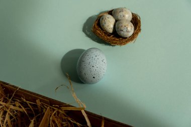 Easter egg on a blue background and and three small blue eggs in the nest