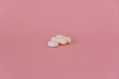Üç beyaz tablet, pembe arka planda vitamin hapları.