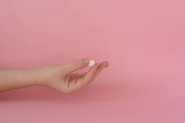 Kadının elindeki vitamin tableti, pembe arka plan.