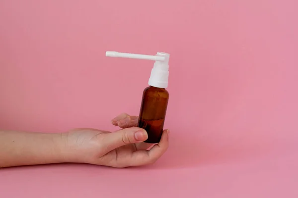 Bottle with medicine throat spray in hand, pink background