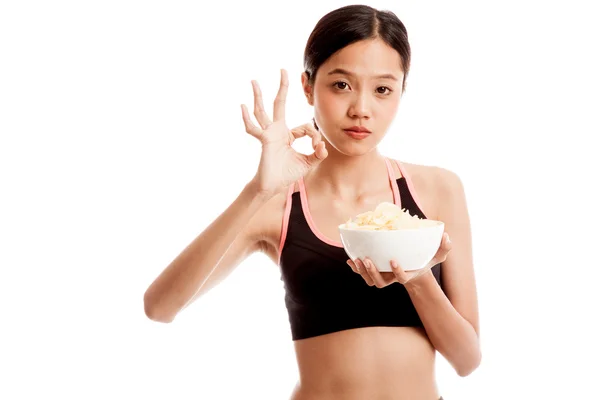 Красивая азиатская здоровая девушка ест картофельные чипсы показать ОК знак — стоковое фото