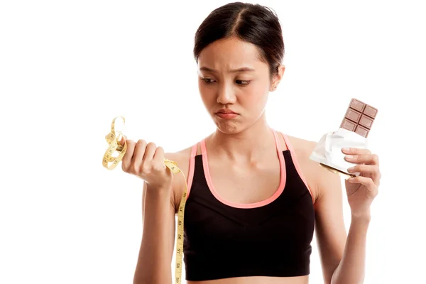 Несчастная азиатская здоровая девушка с шоколадом и измерительной лентой — стоковое фото