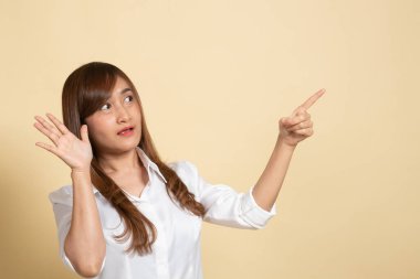 Heyecanlı Asyalı kadın bej arkaplandaki boşluğu işaret ediyor