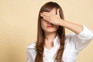 Genç Asyalı kadın bej arka planda ellerini kapatıyor.