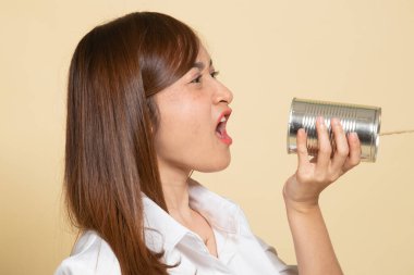 Genç Asyalı kadın bej arka planda teneke bir telefonla bağırıyor.