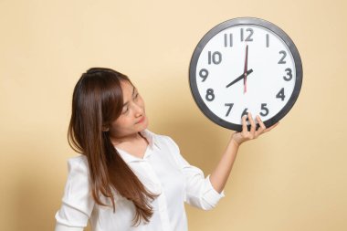 Bej arka planda saati olan genç bir Asyalı kadın.