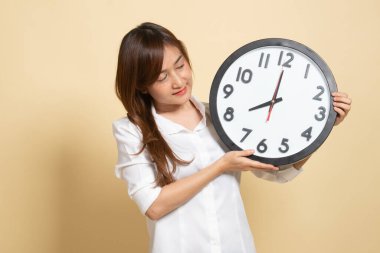 Bej arka planda saati olan genç bir Asyalı kadın.