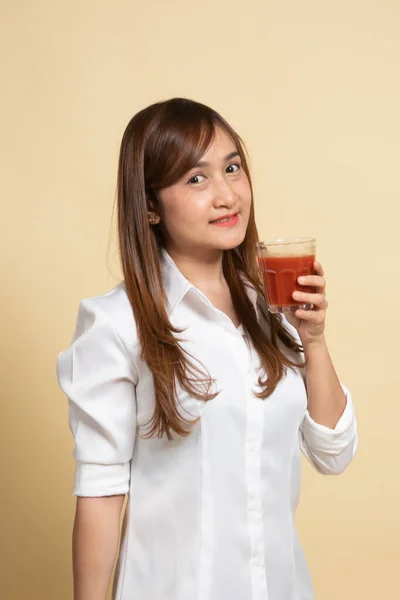 年轻的亚洲女人喝米黄色背景的番茄汁 — 图库照片