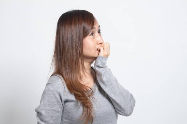 Tereddütlü genç Asyalı kadın beyaz arka planda tırnaklarını yiyor.