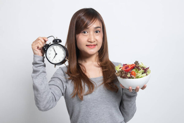 Young Asian woman with clock and salad on white background