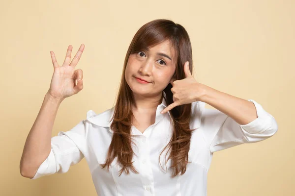 年轻的亚洲女人带着电话手势和米色背景的签名出现在节目中 — 图库照片