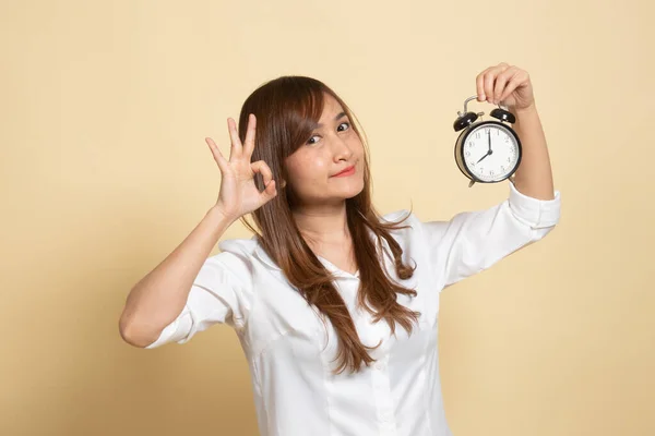 年轻的亚洲女人带着一个米色背景的时钟 表现得很好 — 图库照片