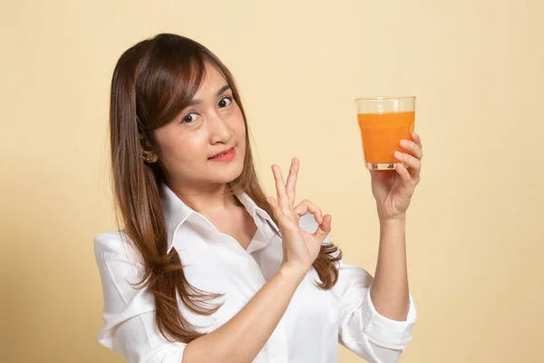年轻的亚洲女人可以在米色背景下喝橙汁 — 图库照片