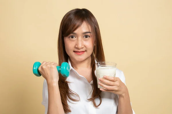 健康的亚洲女人在米色背景下喝一杯牛奶和哑铃 — 图库照片
