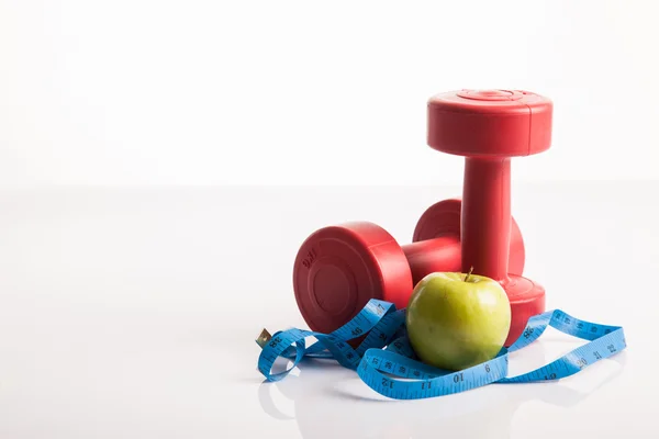 Peso de las pesas rojas con cinta métrica y manzana verde — Foto de Stock