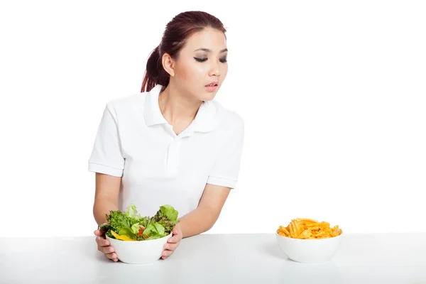 Asiatisk tjej håller sallad men titta på chips — Stockfoto