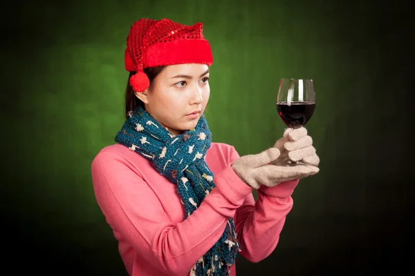 Asiática chica con rojo navidad sombrero mira en vaso de vino — Foto de Stock