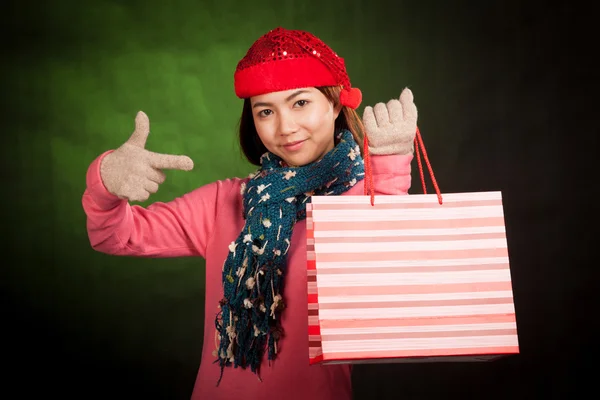 Asiatisk tjej med jul hatt peka på shopping väska — Stockfoto