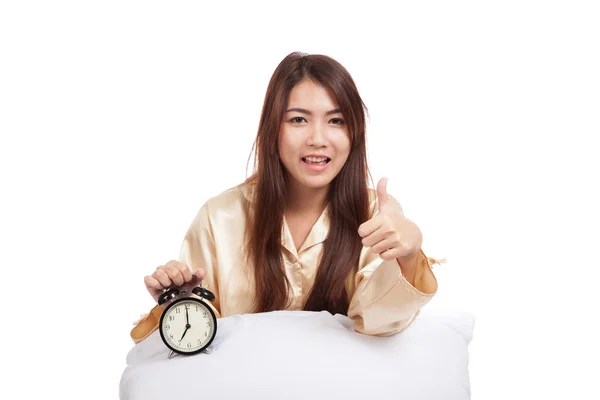快乐的亚洲女孩竖起大拇指与枕头和闹钟 — 图库照片